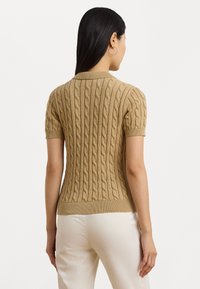 Beige korteblauw kabeltrui met ribbelkraag en -onderrand; de textuurpatroon loopt verticaal over de achterkant.