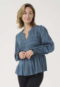 Modrá blúzka so smúteným korzetom, volánovými manžetami a voľným peplum strihom. Hladká tkanina s jemným leskom a okrúhlym výstrihom.