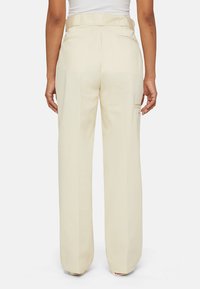 Lichtbeige wijdlopende broek van soepel materiaal, met een achterzak, riemlussen en een subtiele plooi langs het been.