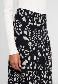 Jupe noire avec un motif animalier blanc, fabriquée en tissu léger. Présente une taille unie et un design plissé.