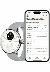 Silberner Edelstahl-Smartwatch mit einem weißen Zifferblatt, grauem Silikonarmband und Gesundheitsdaten, die auf einem benachbarten Smartphone angezeigt werden.