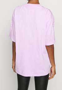 Lilafärgad oversized t-shirt med spetsdetaljer på axlarna, korta ärmar och rak skärning, matchat med svarta leggings.