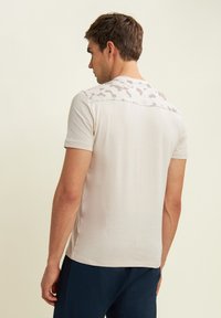T-shirt leggero beige a maniche corte con un motivo camouflage testurizzato nella zona delle spalle, realizzato in un tessuto morbido e con un design aderente.