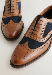Pruun nahk ja tumesinine suede wingtip kingad perforatsioonide, nööride ja ümarate varvastega. Vastupidav talla osa, klassikalised disainielemendid.