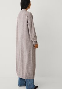 Long, light gray cardigan with a soft texture, ribbed cuffs, and a straight fit, worn over blue flared jeans.