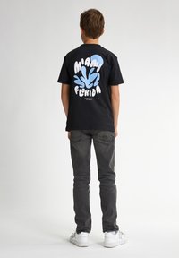 Camiseta negra de algodón con un diseño gráfico azul que incluye el texto "MIAMI" y "FLORIDA". Lleva puesta con jeans grises y zapatillas blancas.