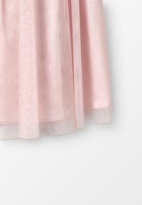 Růžová tylová sukně s vrstveným designem. Má měkkou, průsvitnou texturu s mírně průhledným okrajem. Bez viditelných kovových částí nebo ozdob.