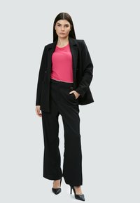 Schwarzer Blazer über einem pinken Hemd, kombiniert mit schwarzen, weit geschnittenen Hosen und schwarzen, spitzen Absätzen; glattes Material mit maßgeschneiderten Linien und Akzenten.