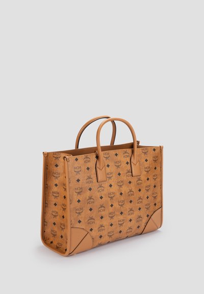 Sac cabas en cuir tanné avec double poignée, présentant des logos MCM noirs répétés et des motifs de losange sur tous les côtés.