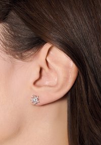 Srebrne kolczyki w kształcie stylizowanego kwiatu z przezroczystymi kryształami, charakteryzujące się szczegółowym, teksturowanym wzorem i wypolerowanym wykończeniem.