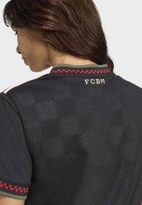 Čierny atletický dres s kockovaným červeným lemovaním a zeleným golierom. Zadná strana obsahuje 'FCBM' v krémovom písmene a jemnú vzorovanú textúru.