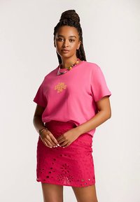 Różowy bawełniany t-shirt z nadrukiem "Like Locals Do" w kolorze żółtym. Połączony z różową koronkową spódnicą z wyciętymi kwiatowymi wzorami.