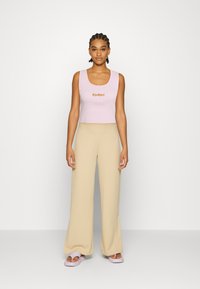 Top cropped em rosa claro canelado com logótipo "Kickers", combinado com calças largas em bege e sandálias de deslize em lilás claro. Texturas suaves e design ajustado.