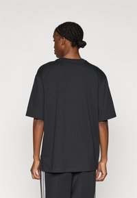 Μαύρο υπερμεγέθες μπλουζάκι με στρογγυλή λαιμόκοψη, κοντά μανίκια και λεία υφή. Φορεμένο με αντίστοιχο σκούρο παντελόνι που έχει λευκές ρίγες.