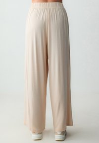 Beige wijde broek met een elastische tailleband, gemaakt van lichtgewicht materiaal. Ze hebben een gladde textuur en vloeien tot de grond.