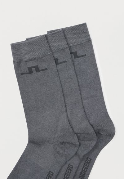Τρία ζευγάρια διπλωμένες σκούρες γκρι κάλτσες πλήρους μήκους με μαύρο γεωμετρικό λογότυπο κοντά στη μανσέτα και κείμενο κατά μήκος της άκρης του ποδιού.