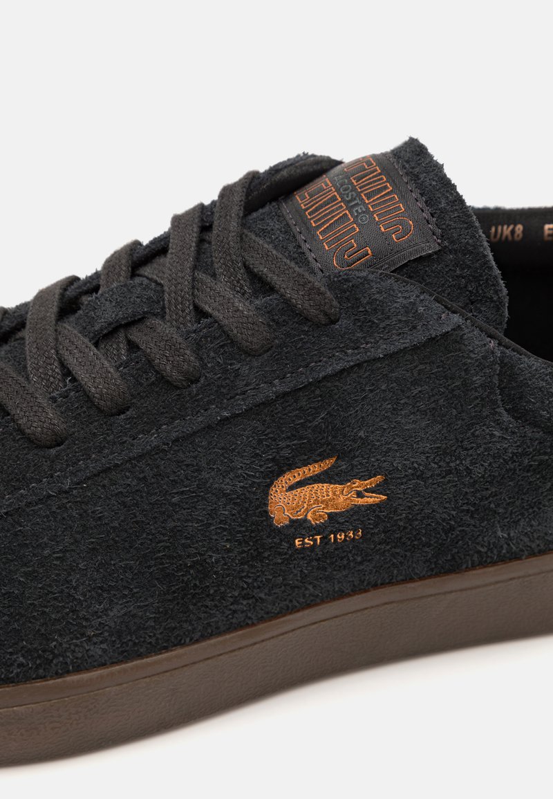 Sneakers in suede nero con superficie testurizzata, suola in gomma marrone e logo ricamato arancione con dettaglio "EST 1933" sul lato.