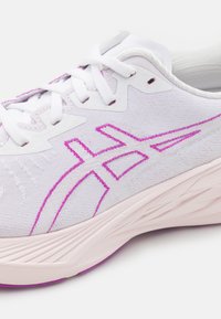 Weiße Sportschuhe mit einer strukturierten Oberseite, rosa gestickten Akzenten, kontrastierenden Schnürsenkeln und einer sich verjüngenden, hellrosa Sohle.