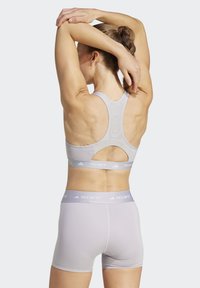 Lichtgrijze sportbeha met uitgesneden rug, elastische band met "TECHFIT"-logo, gecombineerd met bijpassende strakke shorts. Glad textuur.
