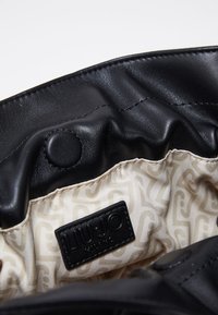 Intérieur de sac en cuir noir avec doublure beige à motifs, comportant une étiquette de marque Liu Jo Milano cousue et un détail de fermeture à bouton-pression.