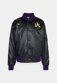 Chaqueta de satén negra con puños y cuello de canalé a rayas en púrpura y dorado, que presenta "LAL" bordado en el lado izquierdo del pecho y un logo de Nike.