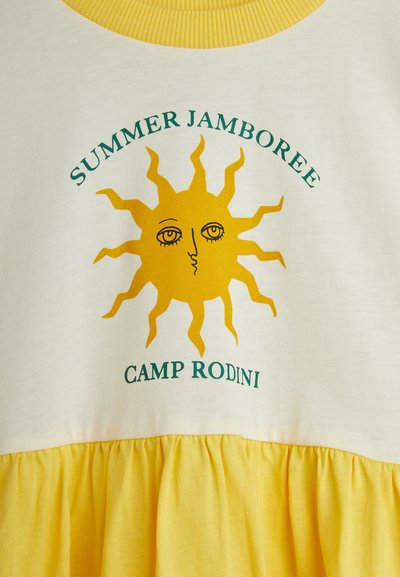 Vestido amarillo y crema que presenta un gráfico de sol con cara, texto "SUMMER JAMBOREE" y "CAMP RODINI", con un dobladillo amarillo fruncido.