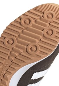 Brown suede shoe sole with a textured gum rubber tread, featuring circular patterns and a white striped accent.