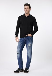 Μαύρο μακρυμάνικο πόλο, τζιν παντελόνι σε μπλε ξεβαμμένο χρώμα με φθορές, μαύρα αθλητικά παπούτσια με άσπρες ρίγες. Εφαρμοστή γραμμή με ριμπ μανσέτες και γιακά.