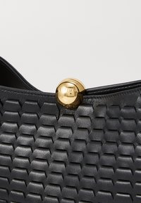 Borsa a tracolla in pelle nera con un motivo esagonale testurizzato. Presenta una chiusura dorata lucida con il nome del marchio inciso. Design semplice ma audace.
