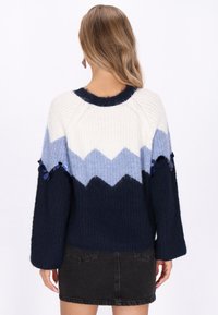 Stickad tr�öja med ett zigzag-mönster i vitt, ljusblått och marinblått, med överdimensionerade ärmar och dekorerade blå paljetter på ärmarna.