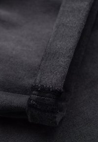 Tela de mezclilla negra con una textura áspera, con un borde doblado que muestra detalles de costura deshilachada y un forro interior suave.