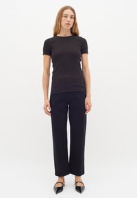 Svart figursydd t-shirt med korta ärmar, kombinerad med högmidjade svarta vida jeans och svarta slingback-skor med spetsig tå. Slät yta.