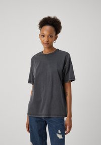 Übergroßes graues Baumwoll-T-Shirt mit Rundhalsausschnitt und kurzen Ärmeln, mit sichtbaren Nähten und einem lockeren Schnitt. Abgewetzte blaue Jeans.