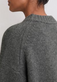 Dunkelgrauer gestrickter Pullover mit gerippter Textur am Kragen und an den Schultern, der einen lässigen, übergroßen Schnitt sowie ein weiches Material aufweist.