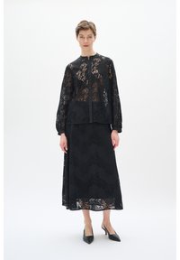Schwarze Spitzenbluse mit langen Ärmeln und Knopfverschluss, kombiniert mit einem passenden schwarzen Spitzenrock. Beide Teile weisen filigrane Blumenmuster auf.