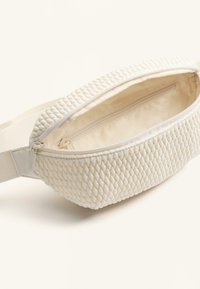 Marsupio bianco intrecciato con esterno testurizzato, forma rettangolare e interno liscio. Presenta un vano principale con zip e una tracolla regolabile.