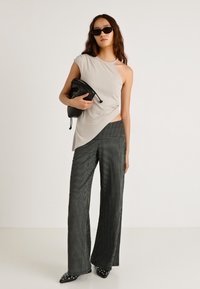 Jasnoszara asymetryczna bluzka w połączeniu z czarnymi szerokimi spodniami w prążki. Modelka trzyma czarną kopertówkę i nosi ciemne okulary przeciwsłoneczne.