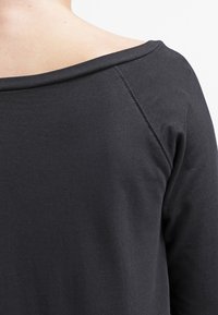 Svart langermet topp med bred, avskjært halslinje. Glatt, mykt bomullsmateriale med raglan-sømmer og minimal sømdetalj.