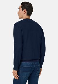 Sweat-shirt bleu marine en tissu tricoté, avec un col rond et des manches longues. Le design est simple avec des poignets et un ourlet côtelés.