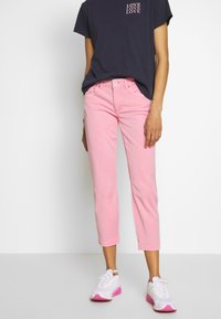 Jean cropped rose clair avec une coupe slim, assorti à un T-shirt bleu marine avec du texte blanc. Baskets blanches avec des accents roses.