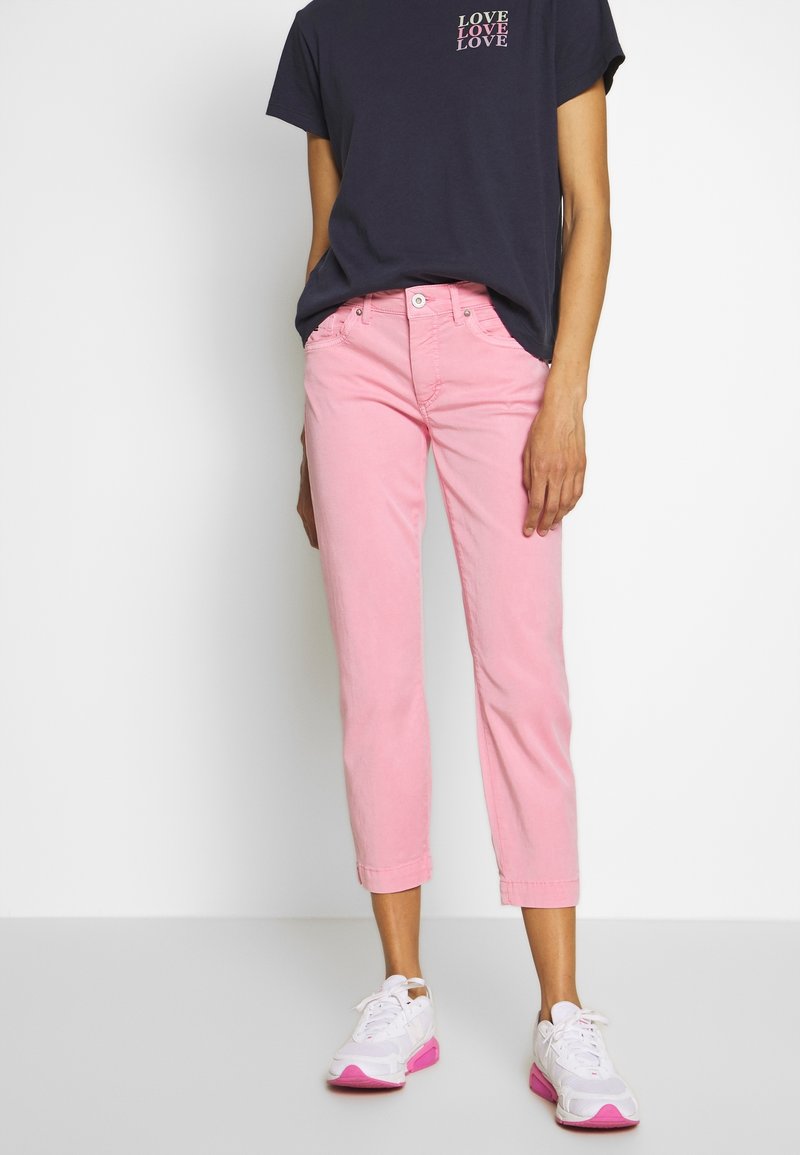 Jean cropped rose clair avec une coupe slim, assorti à un T-shirt bleu marine avec du texte blanc. Baskets blanches avec des accents roses.