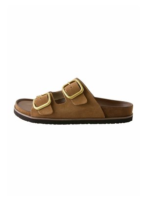 Hnedý semišový šľapák s dvoma nastaviteľnými remienkami so zlatými prackami a čiernou gumovou podrážkou.