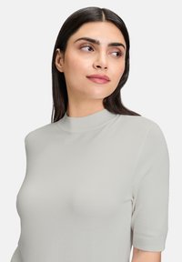 Koszulka z krótkim rękawem w jasnoszarym kolorze, wykonana z dzianiny. Posiada wysoki dekolt i gładką fakturę, z dopasowanym krojem.