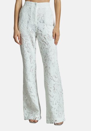 Pantalons évasés en dentelle blanche avec des motifs floraux, taille haute et découpes élaborées, révélant la forme des jambes sous le travail de dentelle.