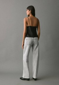 Črna satenska top z tankimi naramnicami, v kombinaciji s svetlo sivo širokimi kavbojkami in črnimi gležnjarji, viden od zadaj.