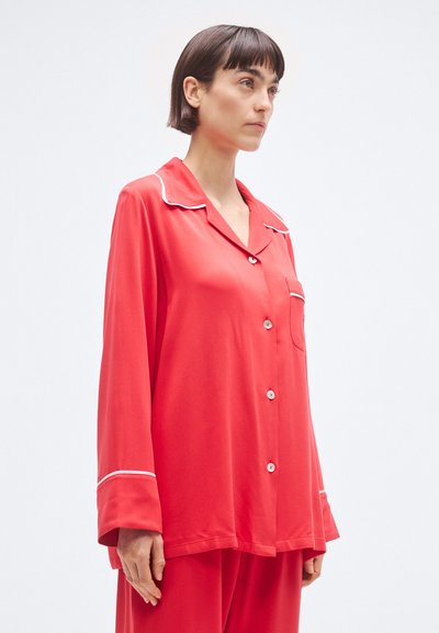 Červená hodvábna saténová pyžamová košeľa s výrezom na klopách, bielym lemovaním, predným vreckom a zapínaním na gombíky. Voľný strih s dlhými rukávmi.