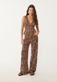 Jumpsuit marrone con motivo floreale, dotato di scollatura a V profonda, gambe larghe e una vestibilità comoda, abbinato a sandali casual.