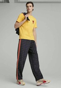 Yellow cotton t-shirt with a red graphic, paired with navy patterned sweatpants featuring orange side stripes and multi-color sneakers.