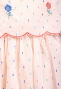 Vyšívané šaty z měkké růžové látky s malými barevnými puntíky. U výstřihu a na volánovém lemu jsou modré a červené květinové motivy.