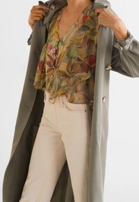 Długa, szałwiowo-zielona kurtka na kwiecistą, wielokolorową bluzkę; zestawiona z jasnymi, dopasowanymi dżinsami oraz guzikami na kurtce.